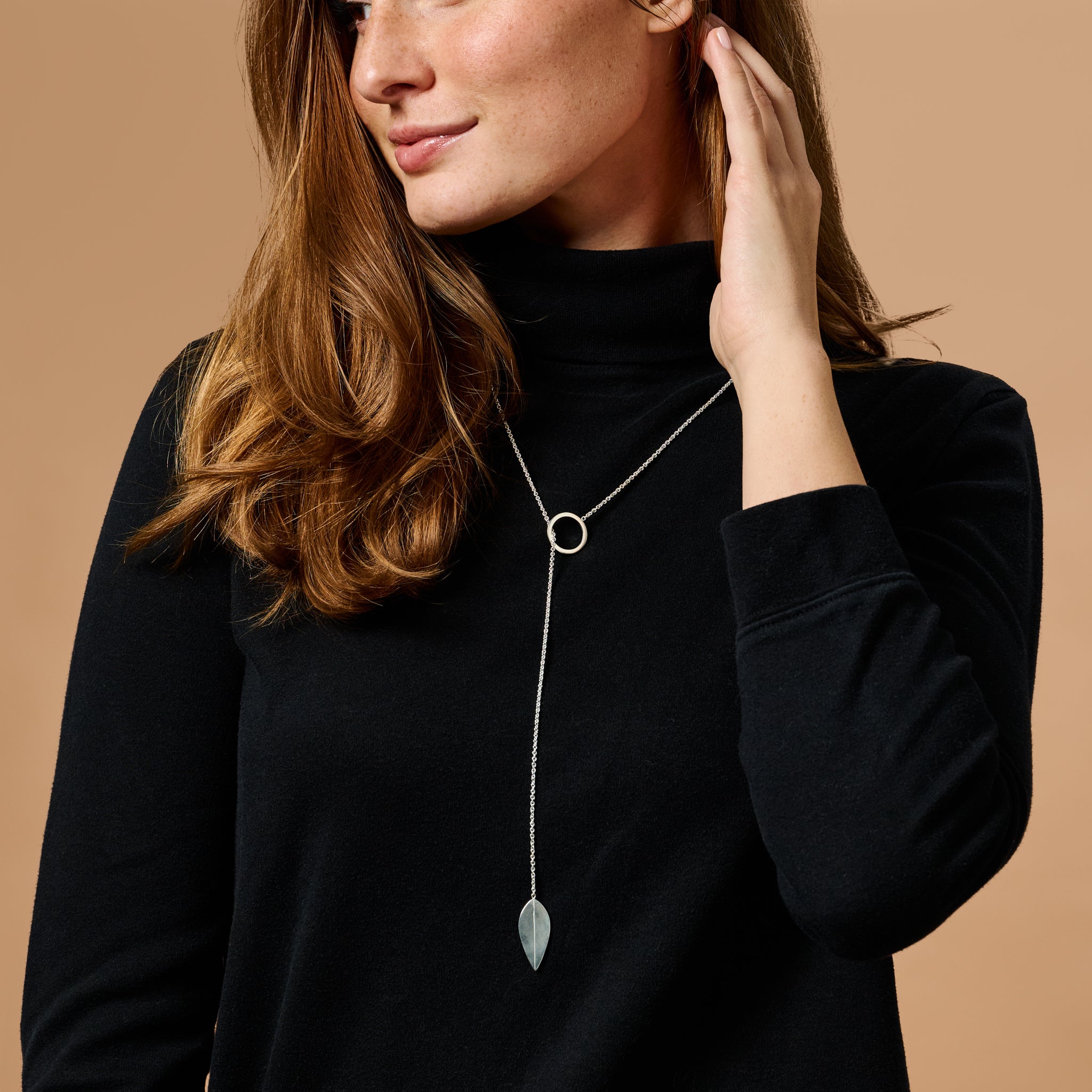 Close-up of silver leaf pendant suspended on lariat chain against white background