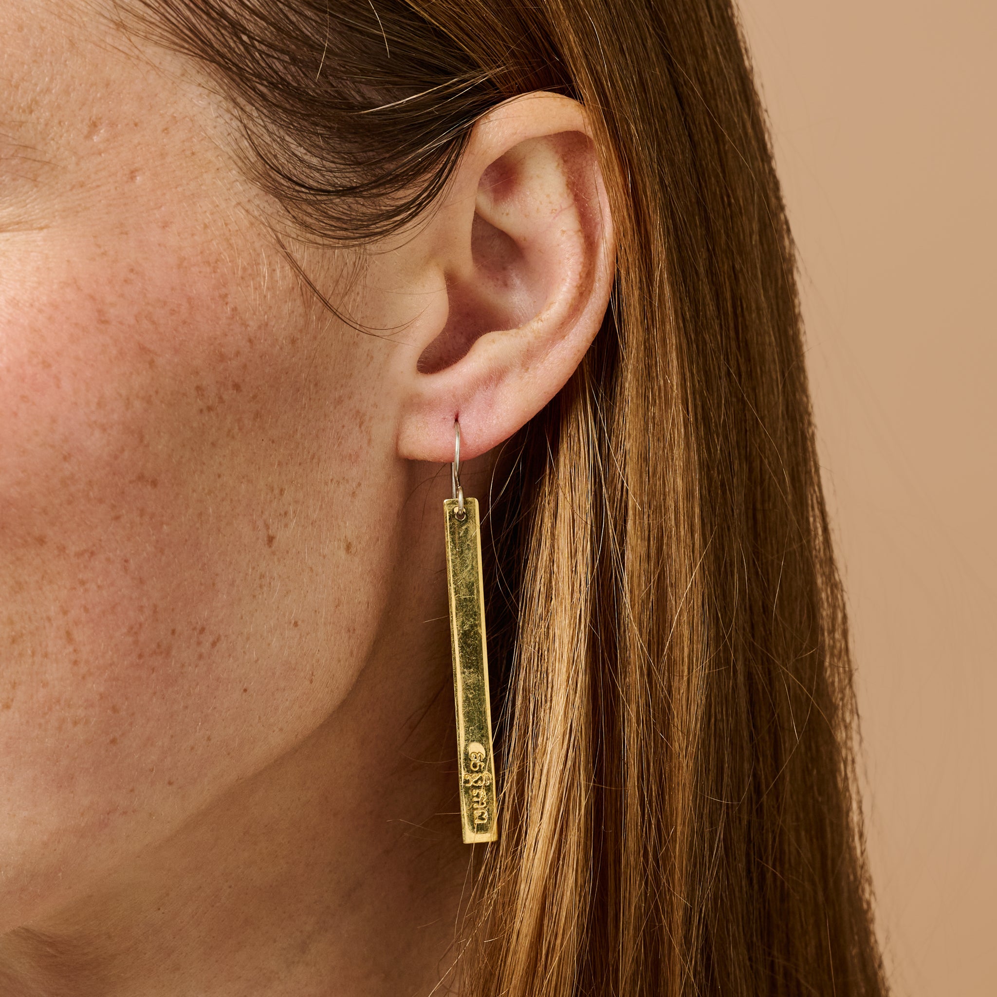 Close-up of Resilient Peace Artisan Earrings highlighting their unique brass craftsmanship.