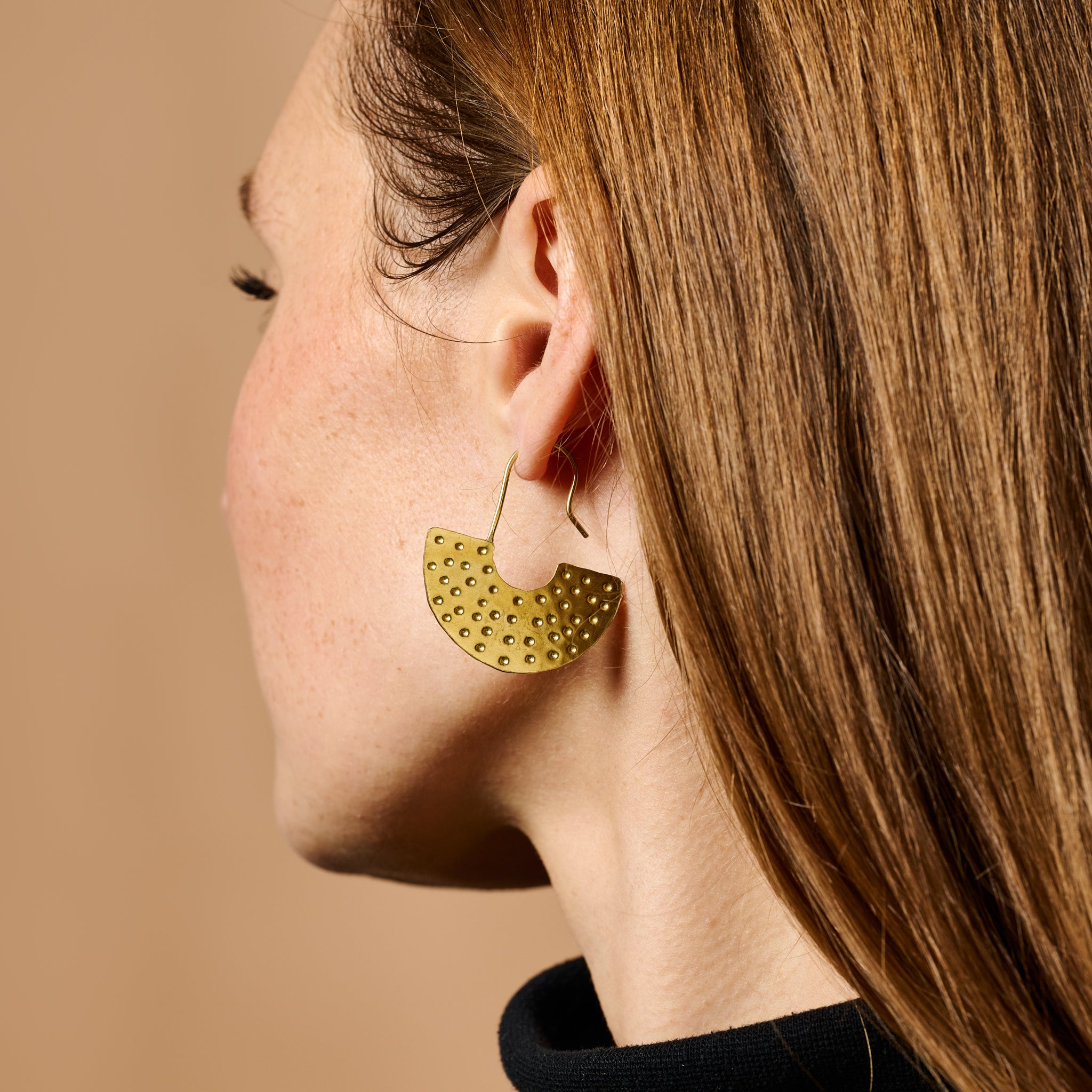 Close-up of handcrafted brass earrings with etched dot pattern, highlighting artisan craftsmanship.