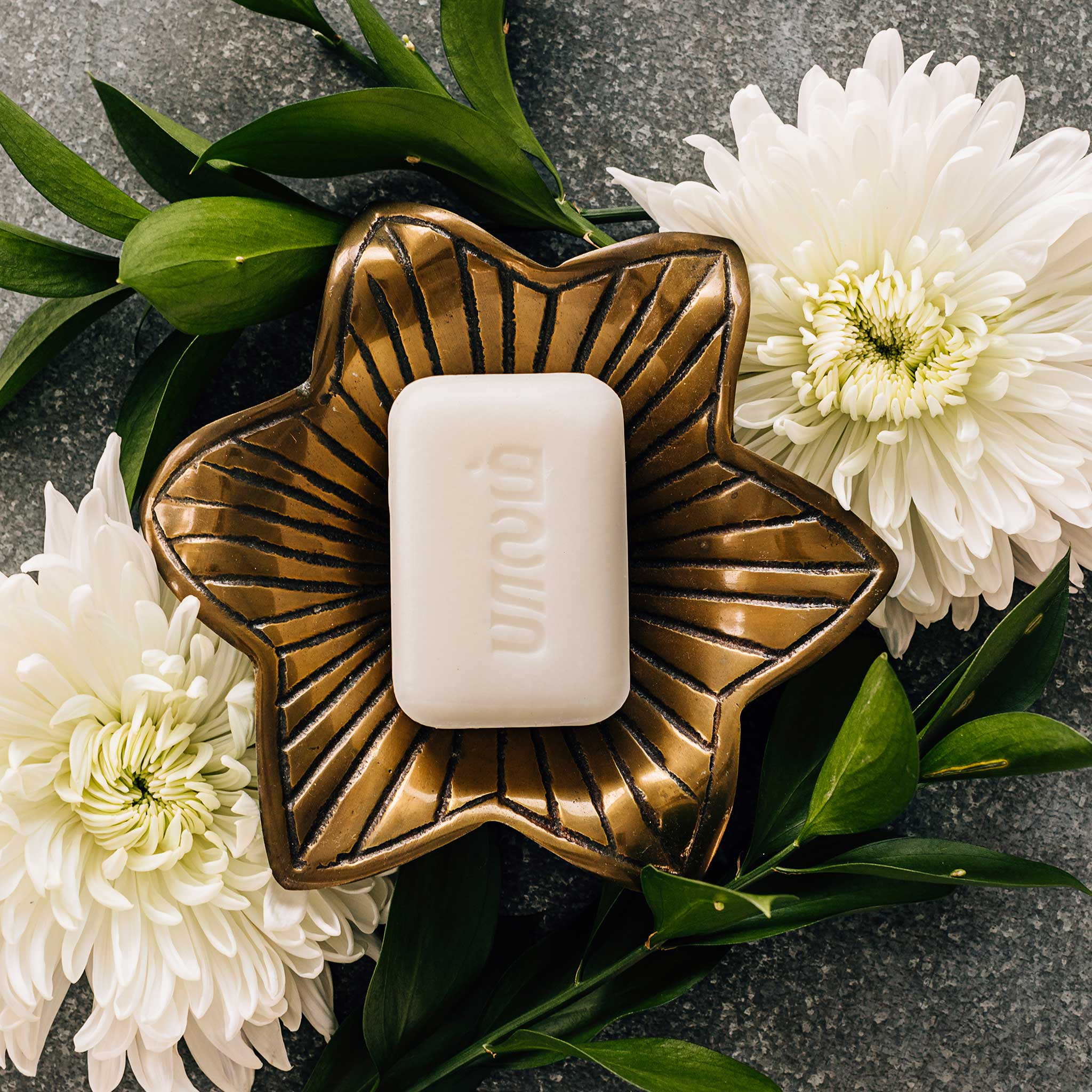 Hand holding Lotus Blossom Natural Soap near a sink for everyday use demonstration.