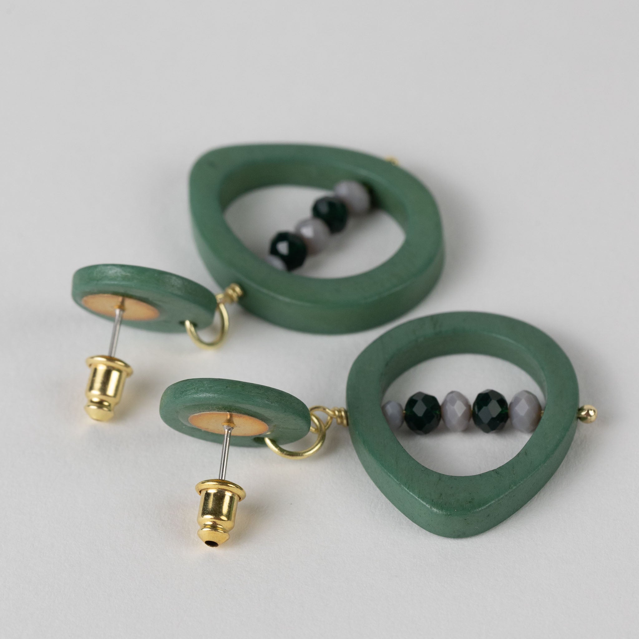 Detail shot of the carved green eyes with dangling glass beads on artisan earrings
