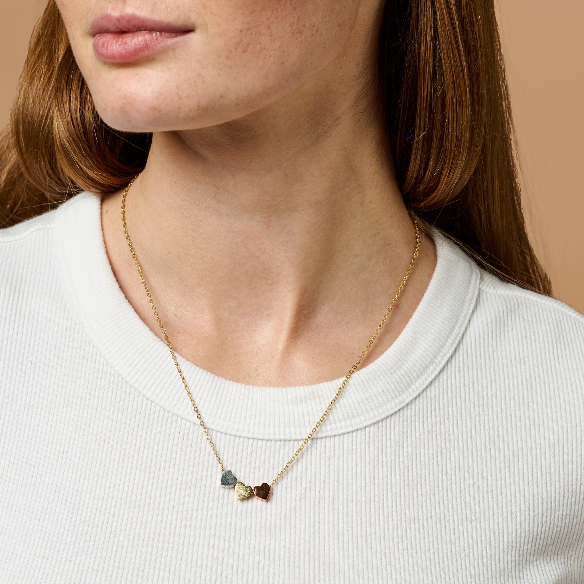 Elegant Triad Heart Necklace showcasing copper, silver, and gold hearts from a side angle.