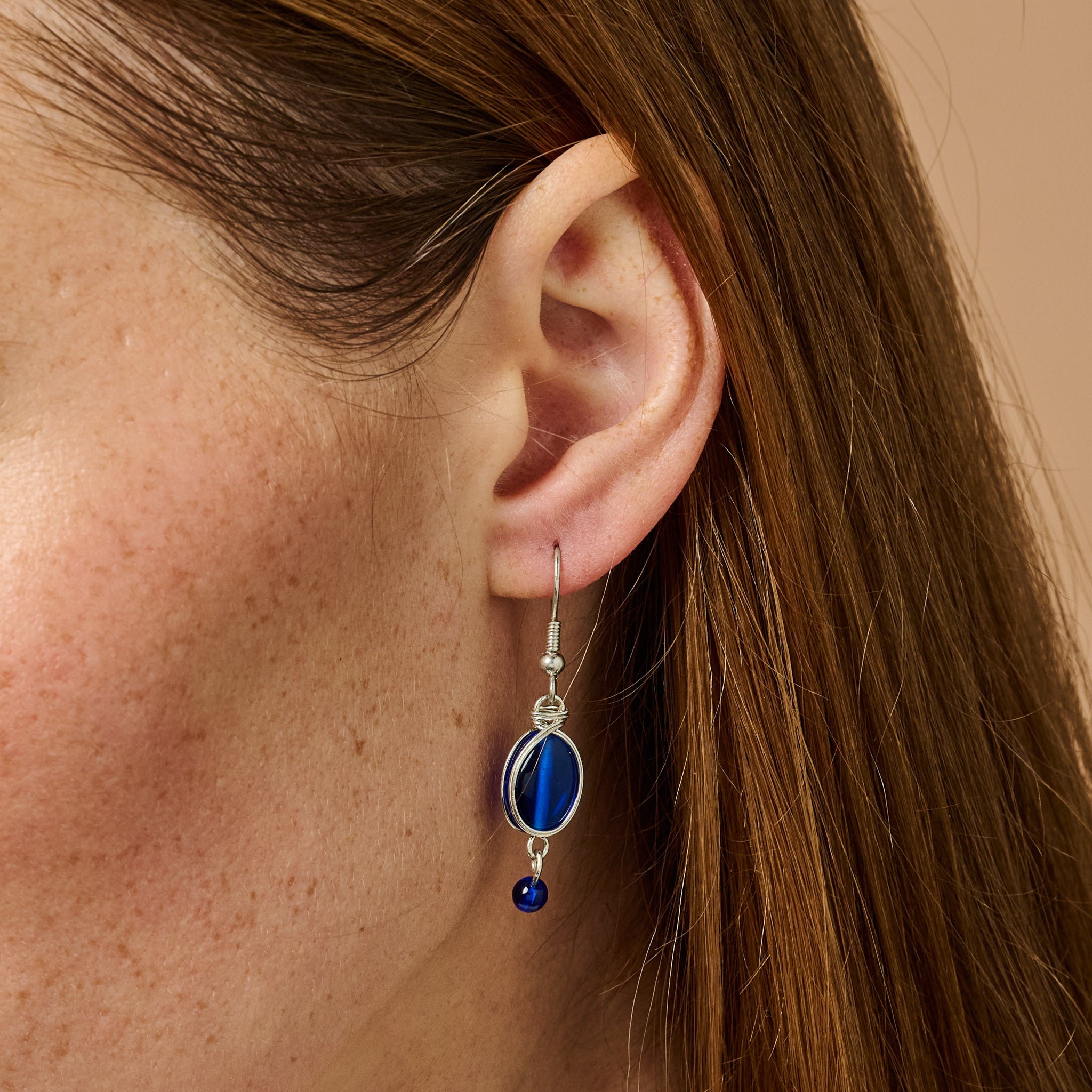 Close-up view of handmade blue glass beaded earrings with white wire wrapping