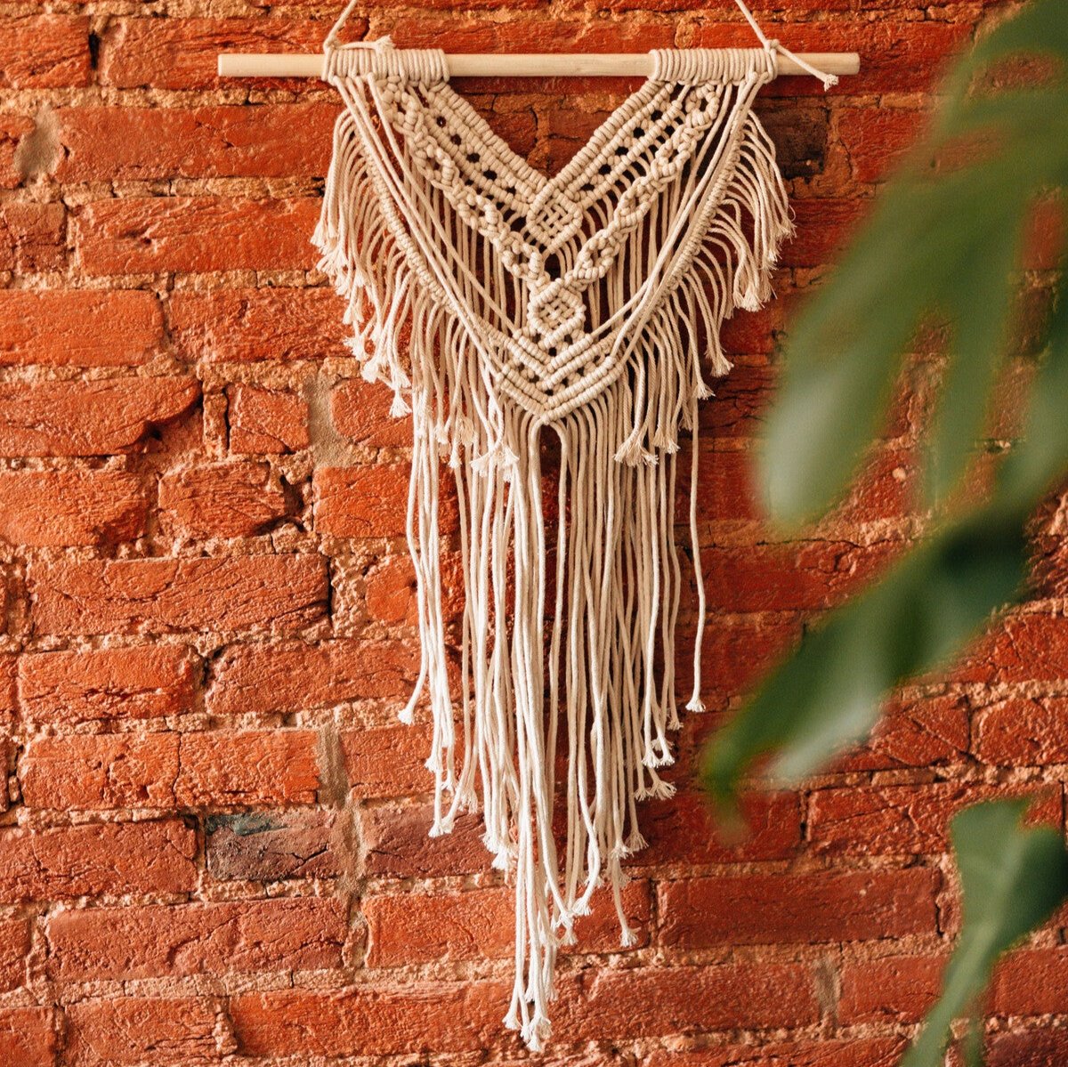 Close-up of cream-colored fiber art wall decor showing tasseled ends