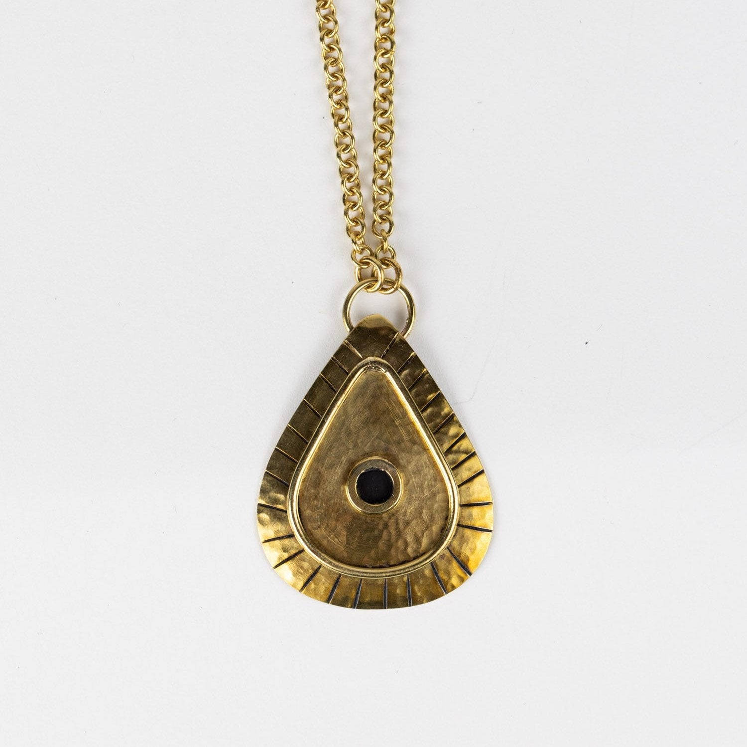Close-up of the hammered brass pendant necklace showing its textured finish and artisan detailing.