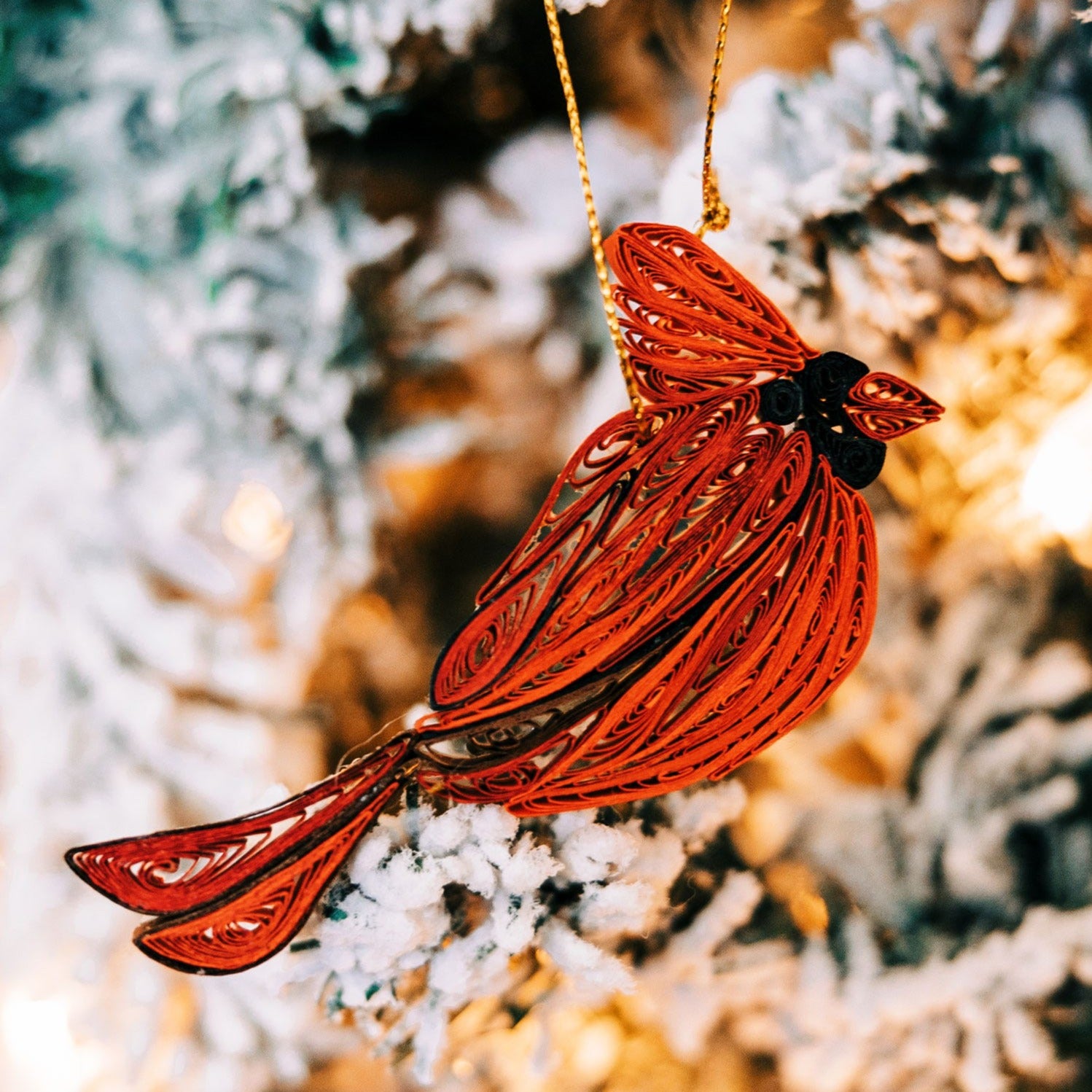 Close-up of a handmade quilled cardinal ornament hanging on a Christmas tree