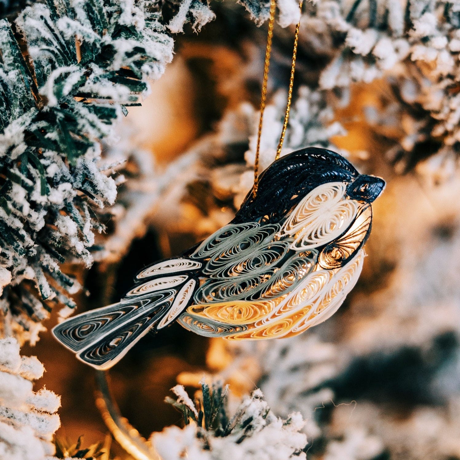 Chickadee ornament with 3D quilled feathers hanging on a Christmas tree.
