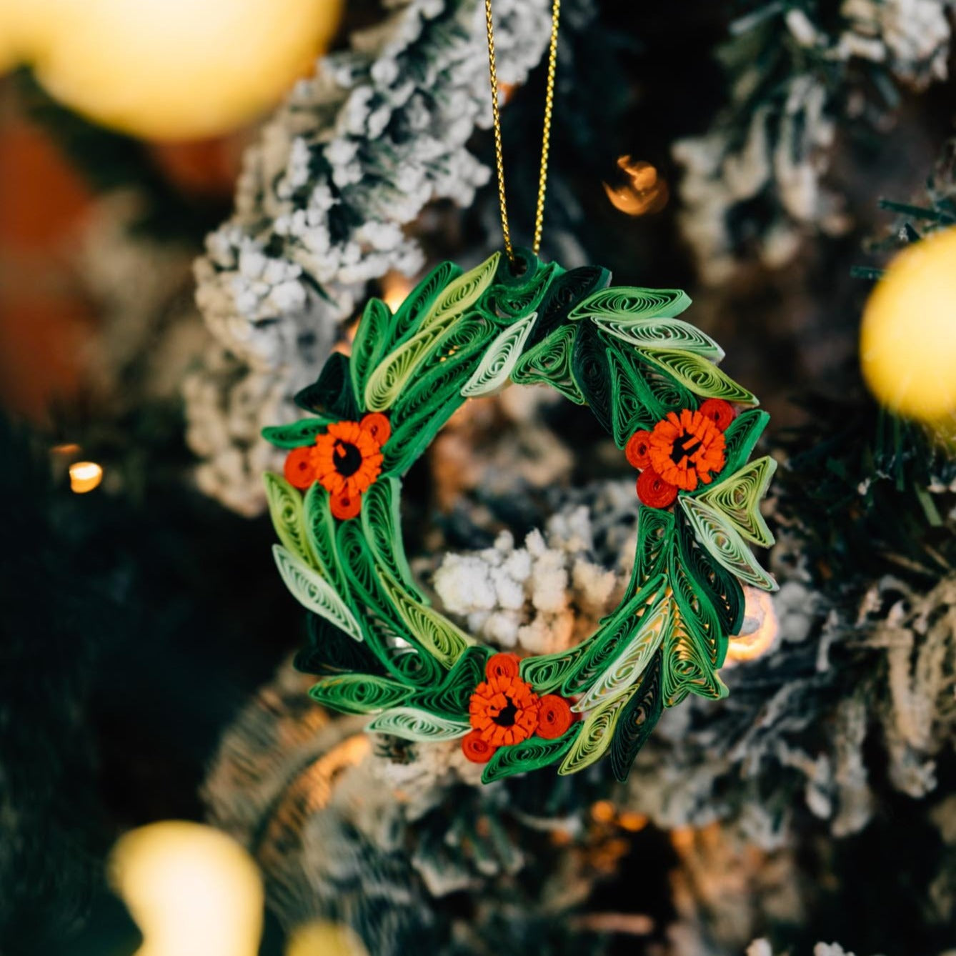 Close-up of exquisite quilled paper wreath ornament hanging on a holiday tree.