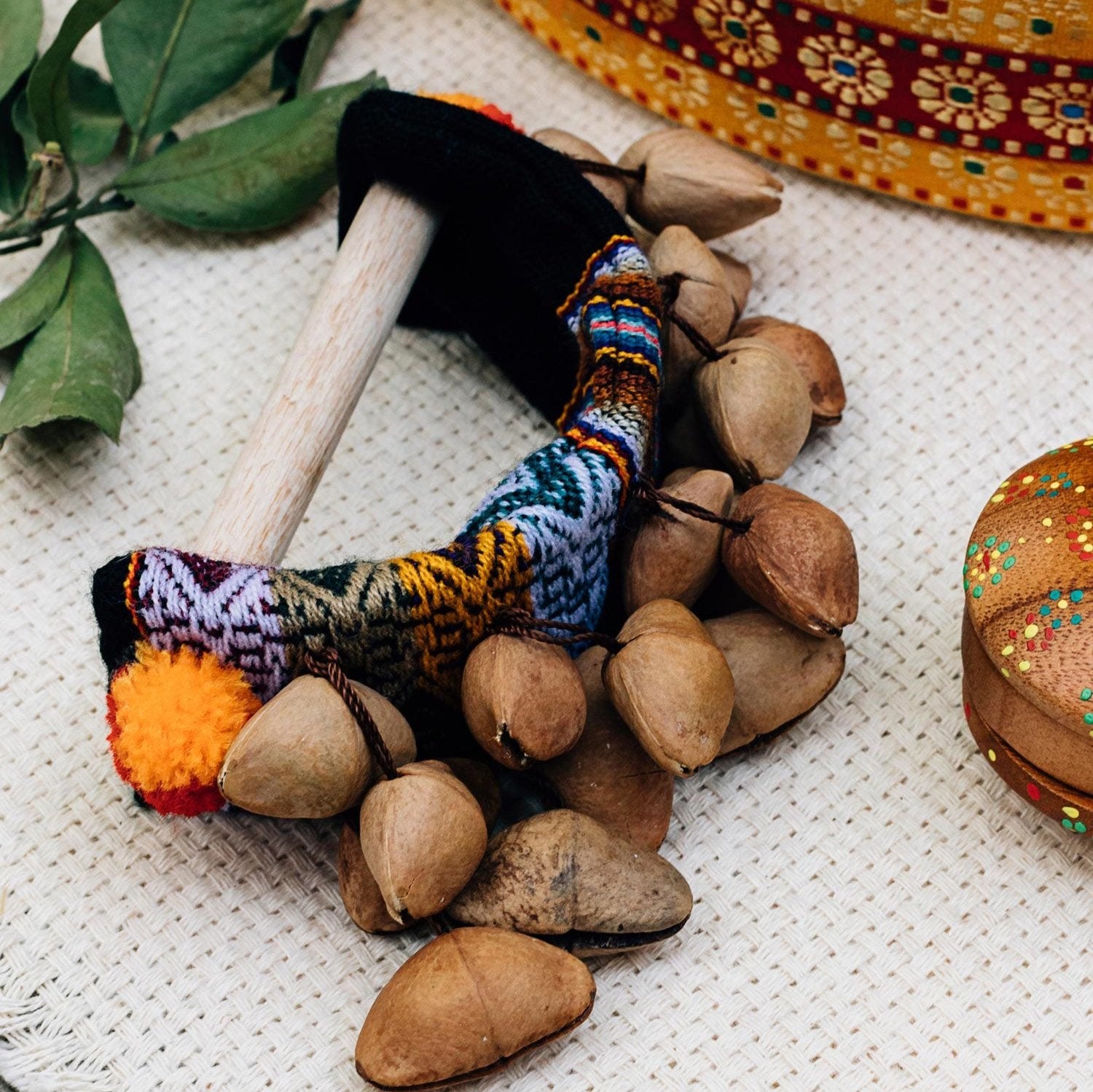 Close-up of the Tanuni Handcrafted Seed Rattle showing its colorful pom poms and natural wood.