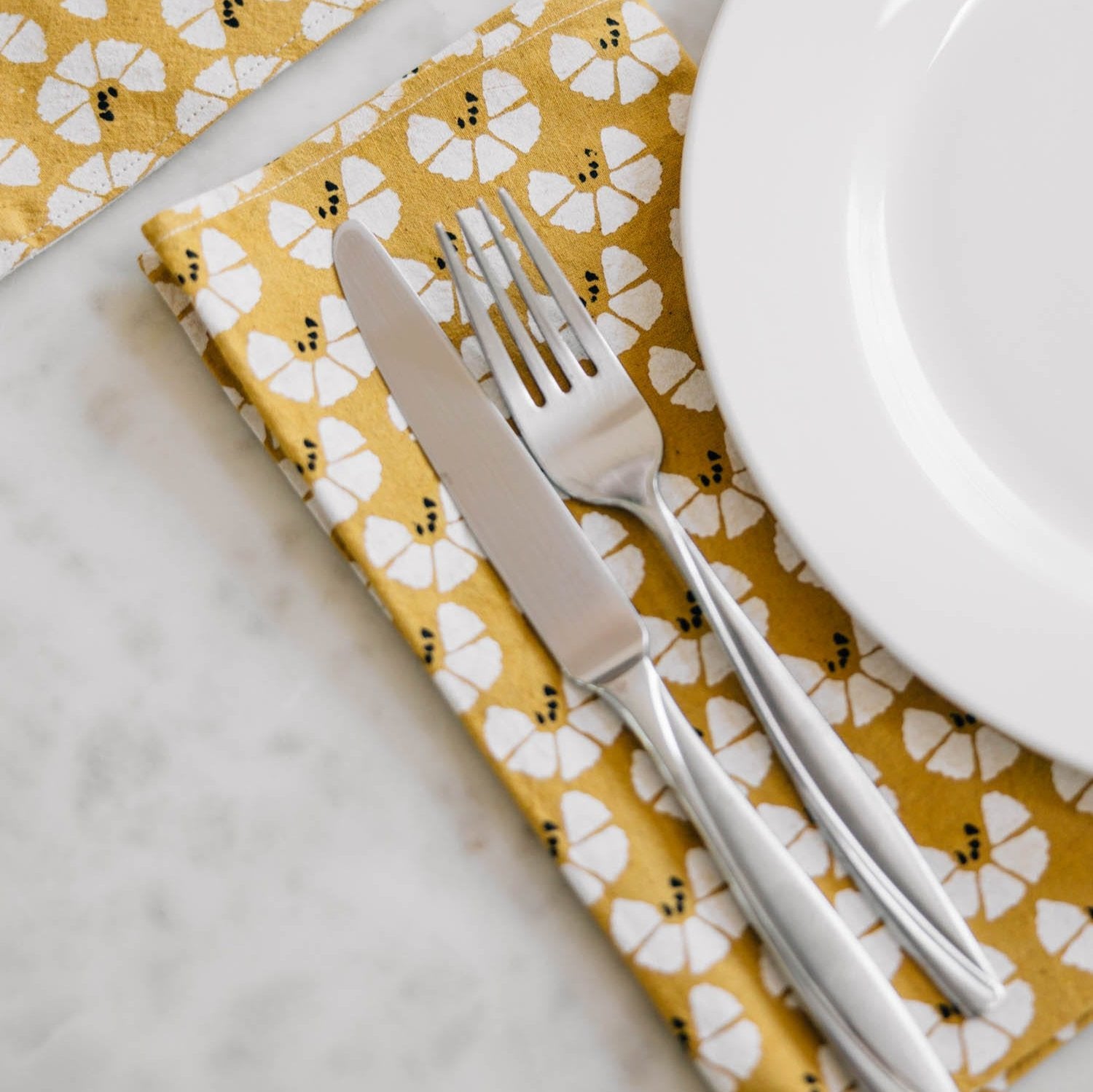 Top-down view of four Quiet Sun napkins folded on a wooden table with rustic tableware