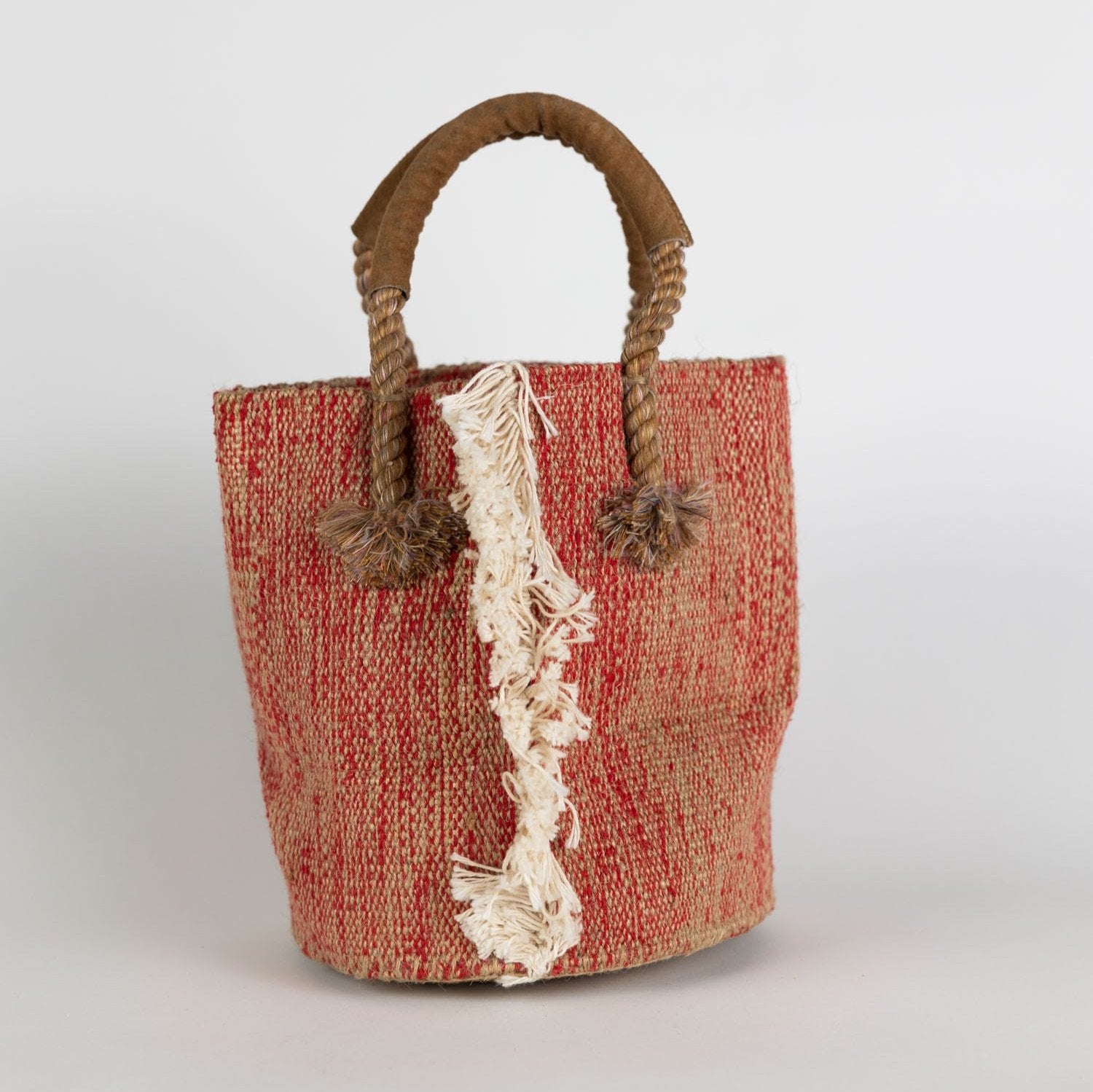 Chic jute cotton bucket bag displayed outdoors with fringe detail, ideal for summer vacations.