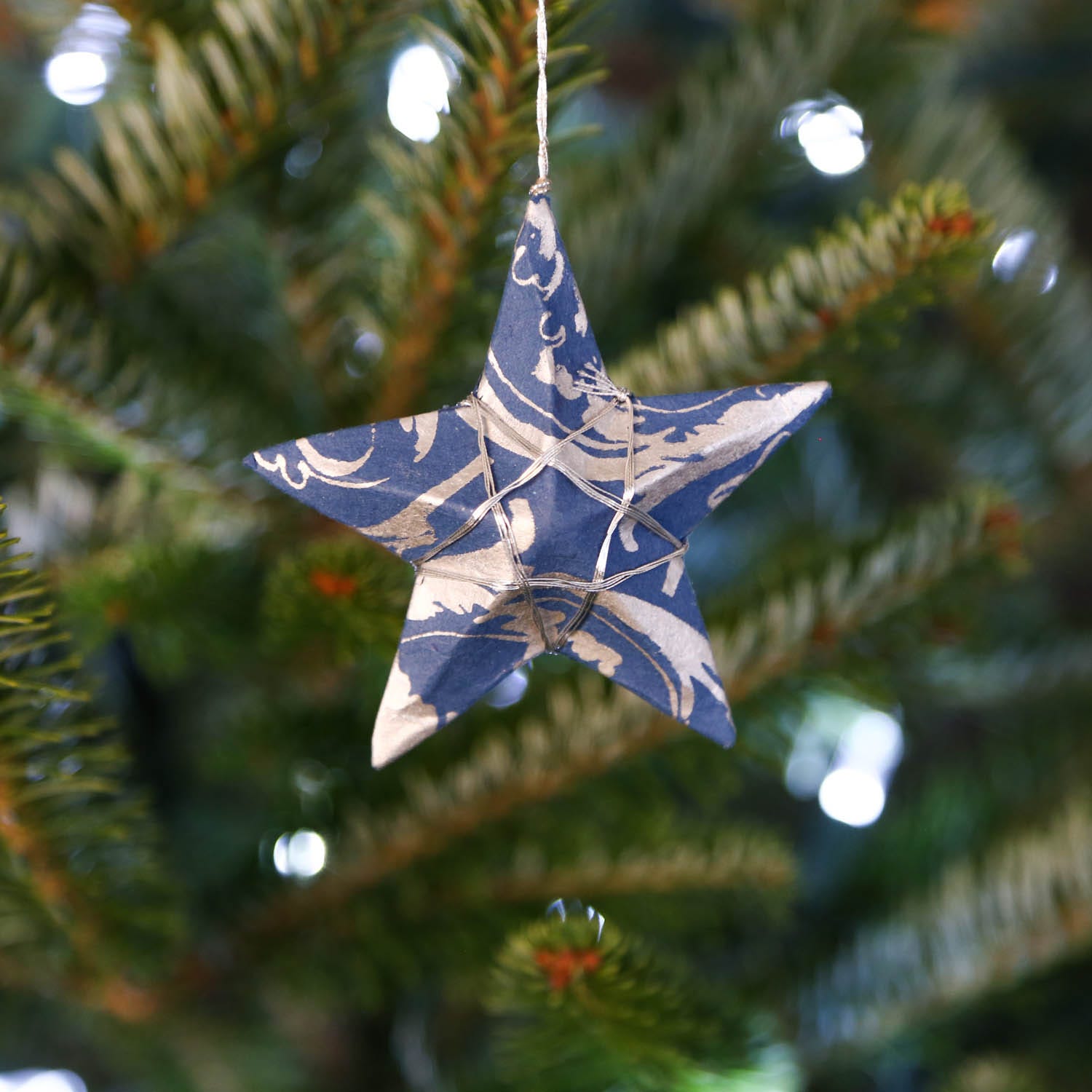 Celestial silver paper star ornament hanging elegantly in a festive setting.