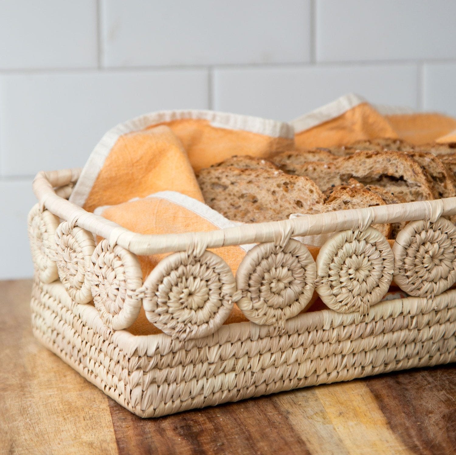 Handwoven palm leaf bread basket displayed with fresh bread and condiments.