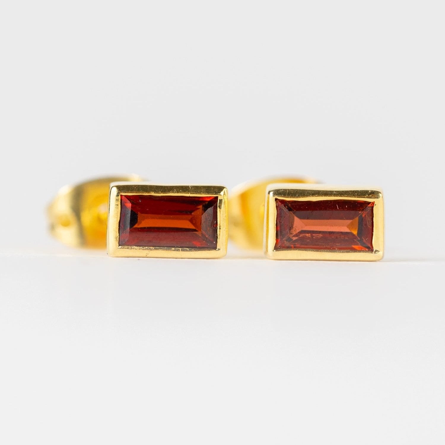 Elegant garnet gold baguette earrings on a display stand