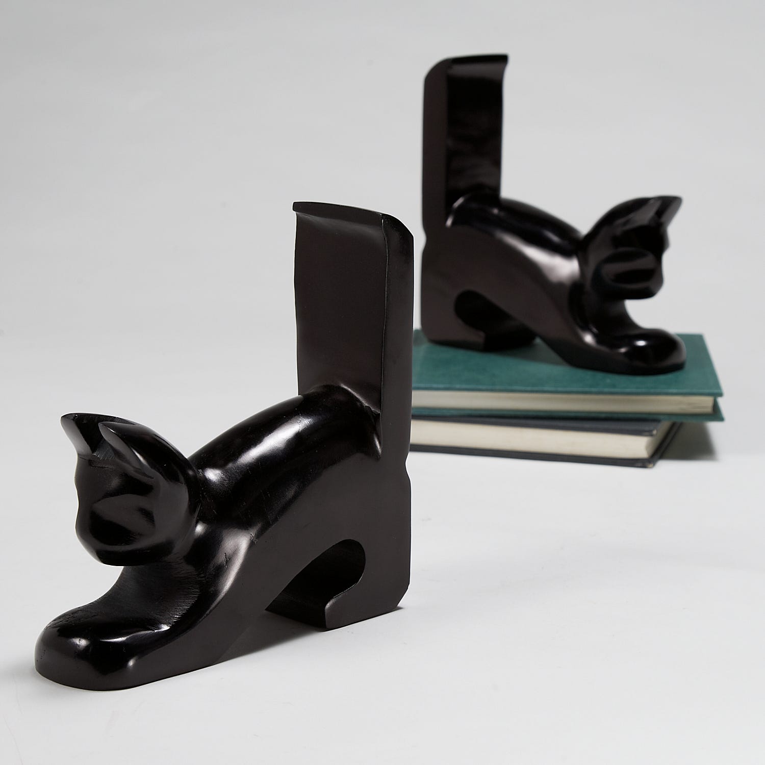 Playful stone cat bookends holding books on a shelf, showing intricate details and craftsmanship.