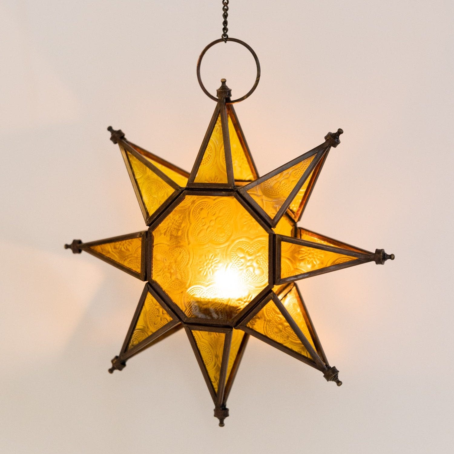 Starlight artisan hanging candle holder showcasing glowing glass and antiqued copper finish from an angle.