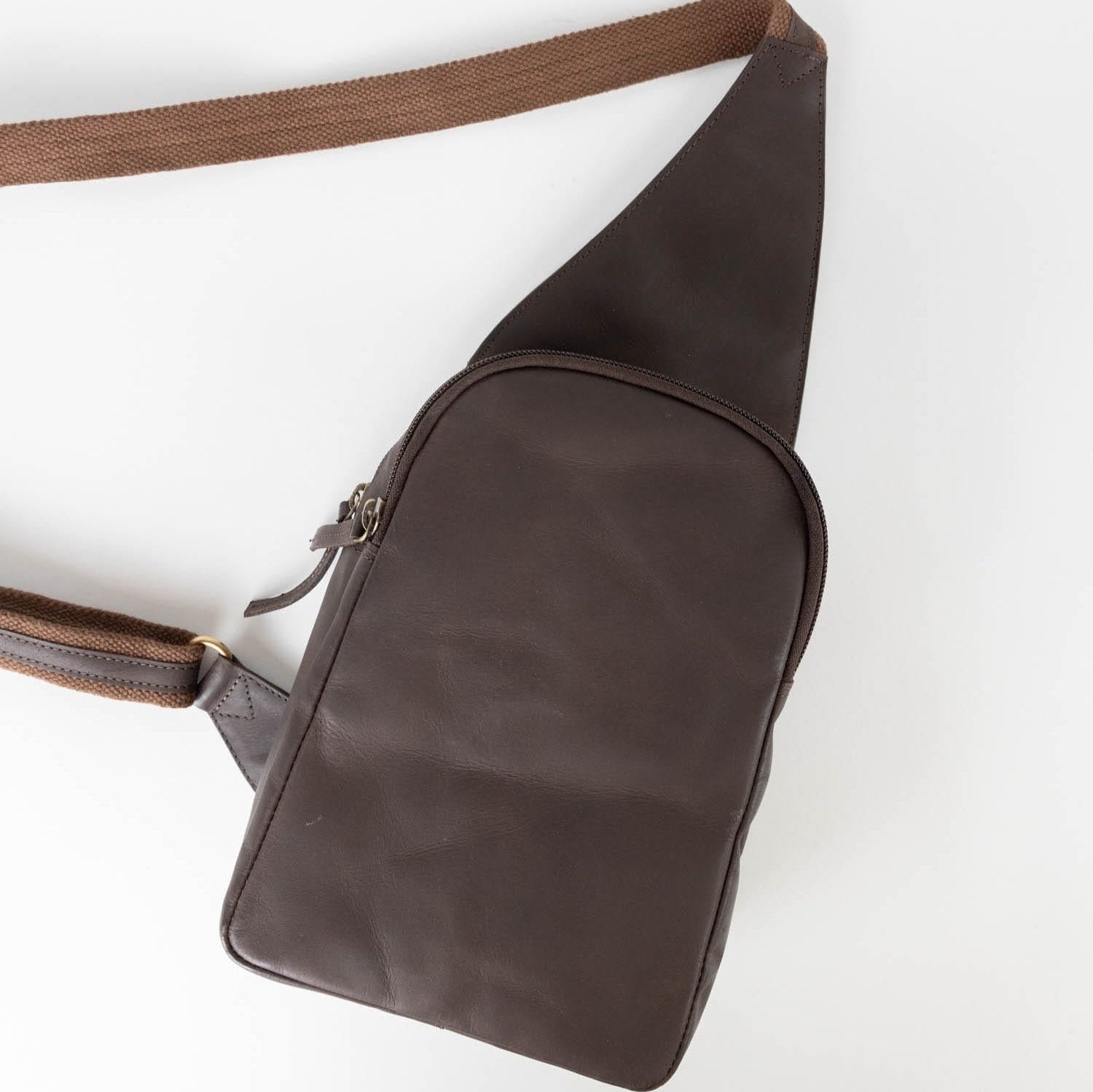 Close-up of the eco-leather sling bag showing its textured dark brown surface and zipper