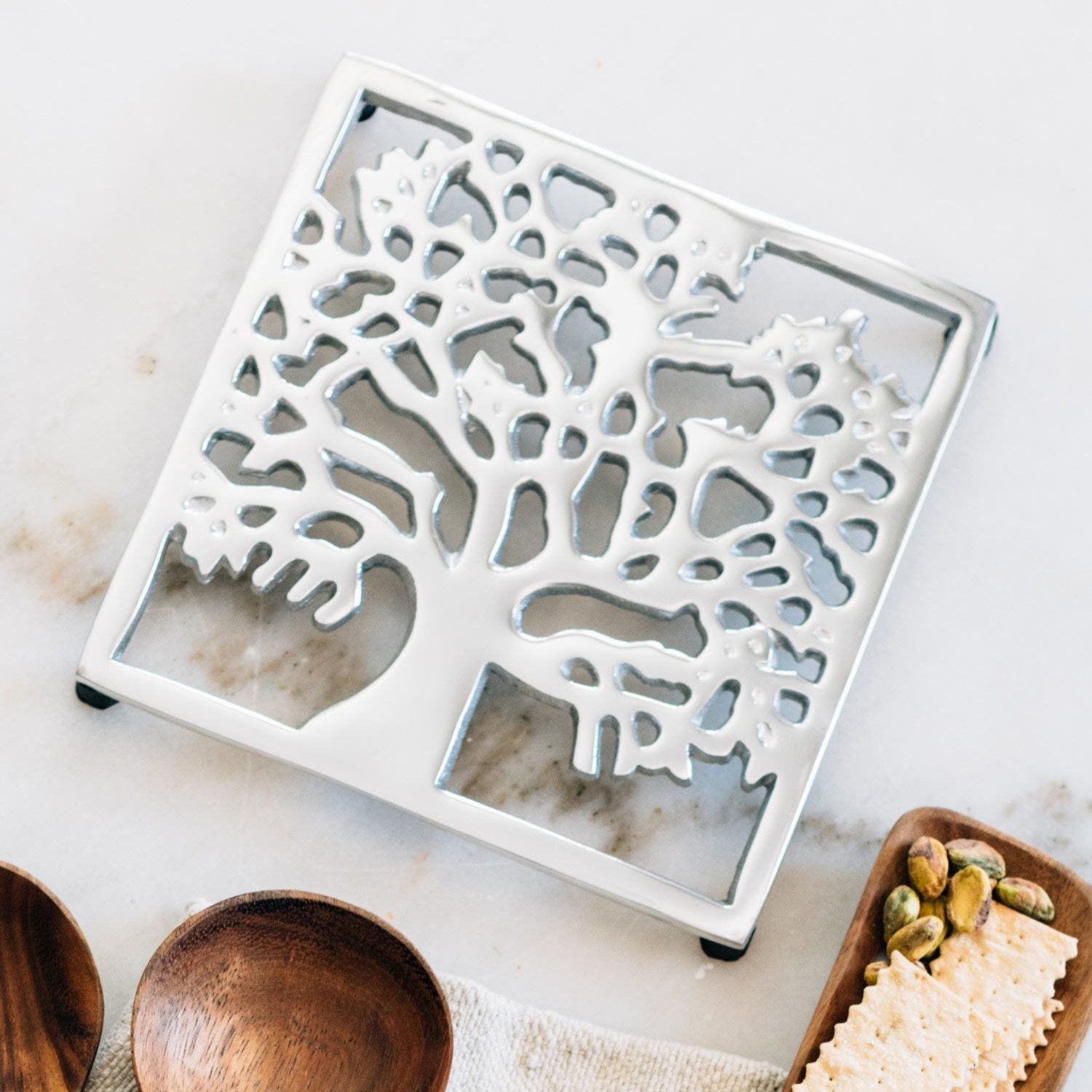 Handcrafted Sheesham tree trivet showing polished silver finish and rubber feet.