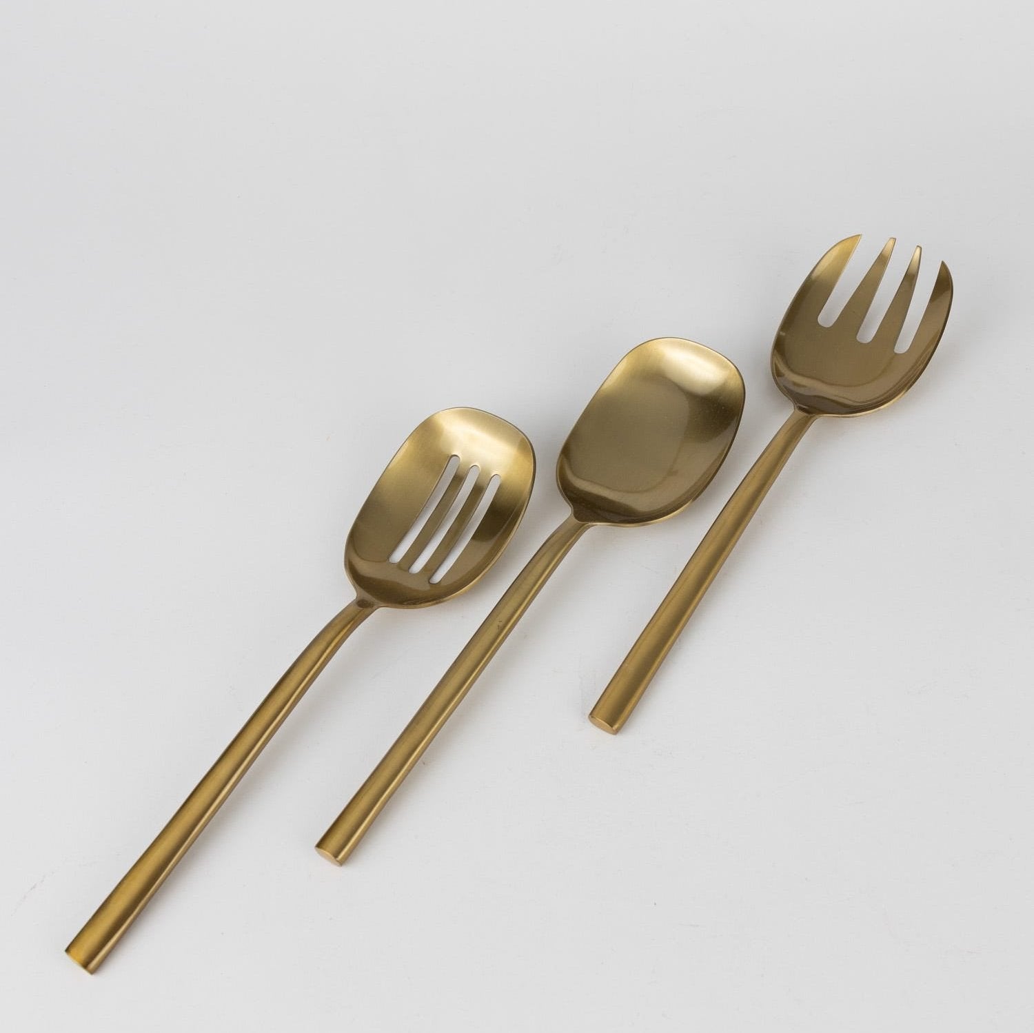 Three elegant brass serving spoons displayed on a dining table, showcasing their unique designs.