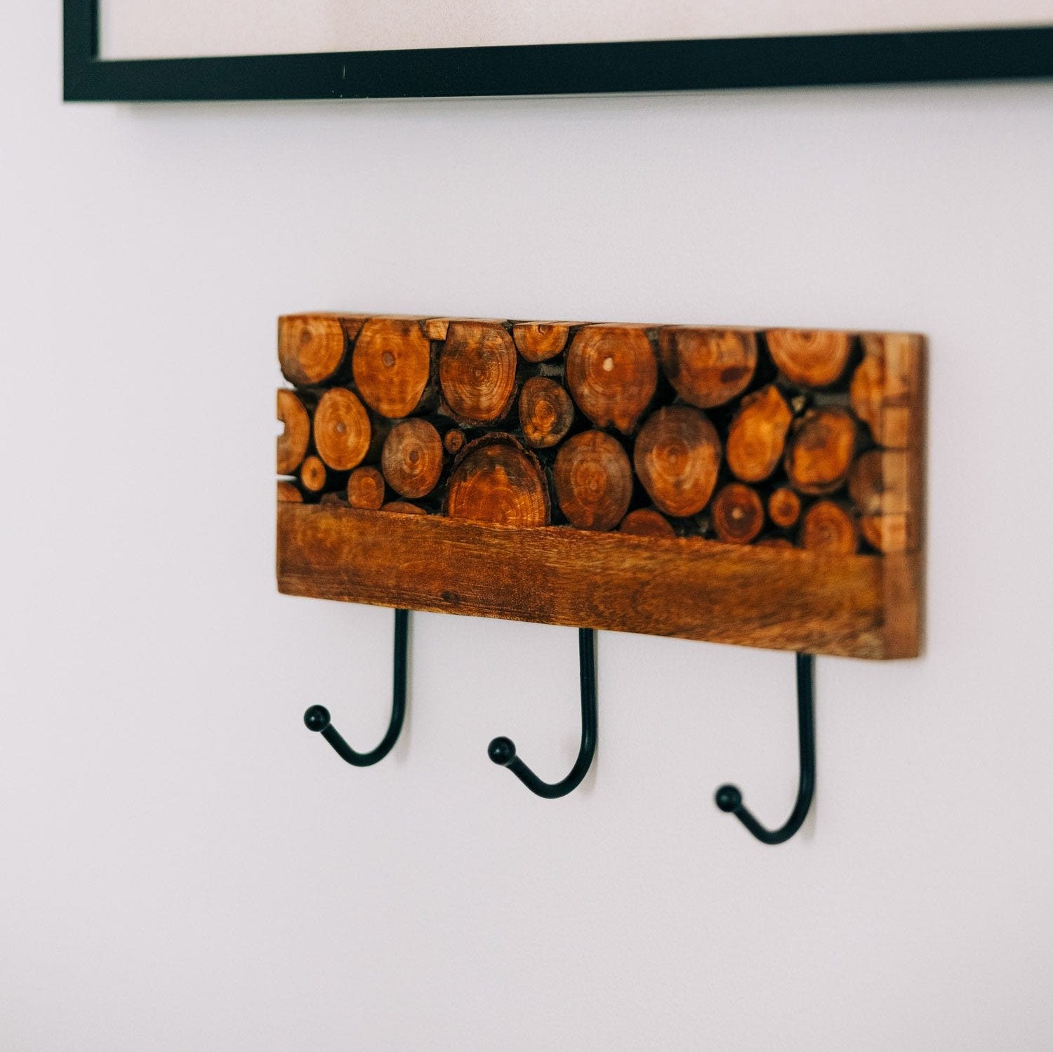 Close-up of handcrafted mango wood slice wall hook with black iron hooks, rustic decor style