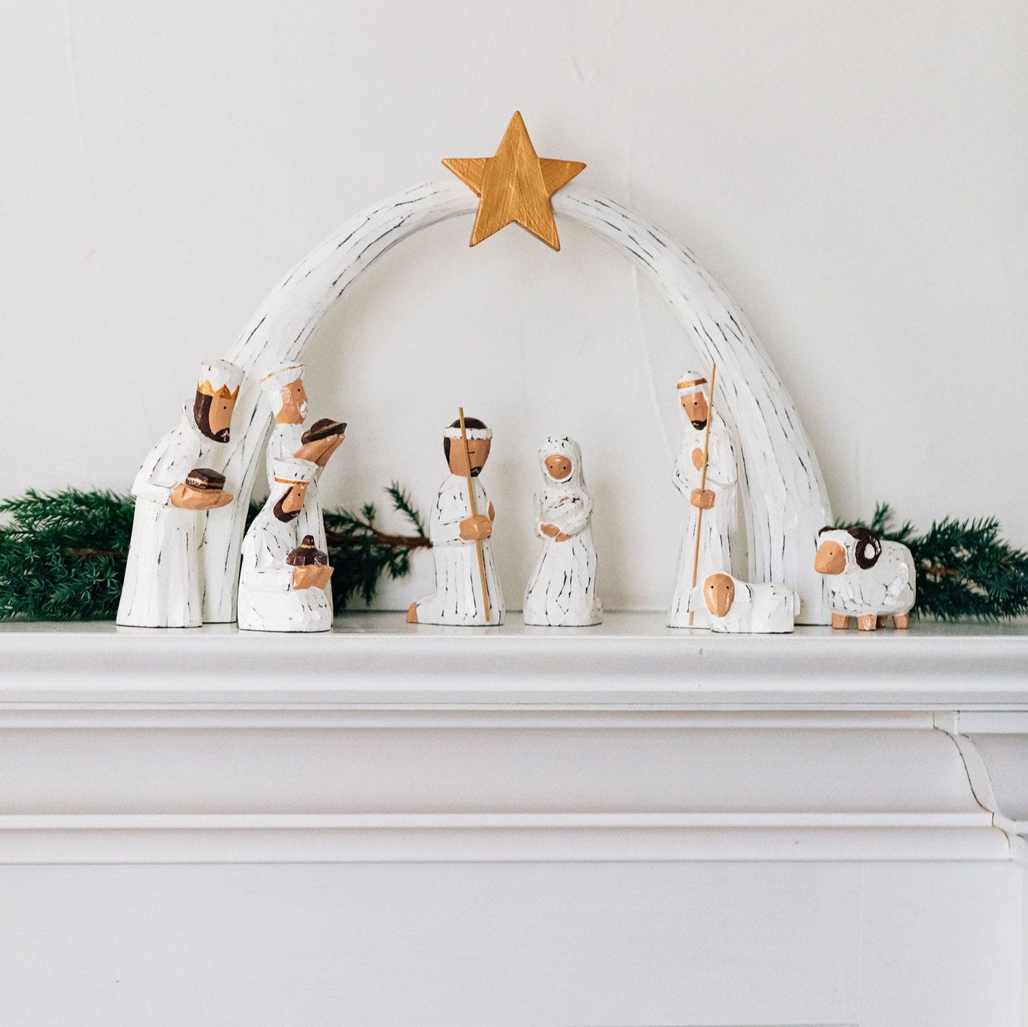 Close-up of handcrafted Albesia wood nativity figures with detailed white and gold painting