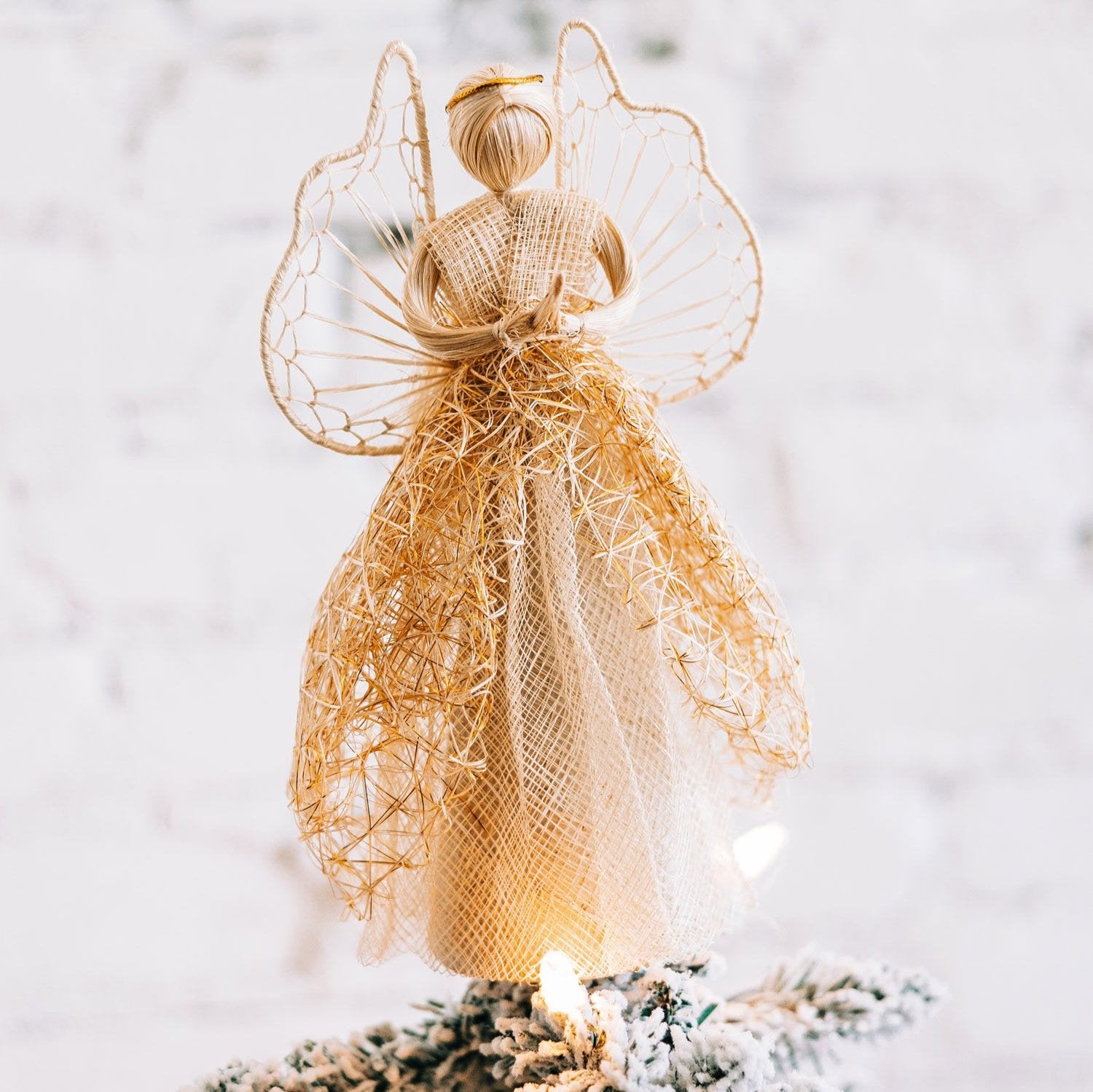Heavenly sinamay angel tree topper with gold accents on a decorated Christmas tree.