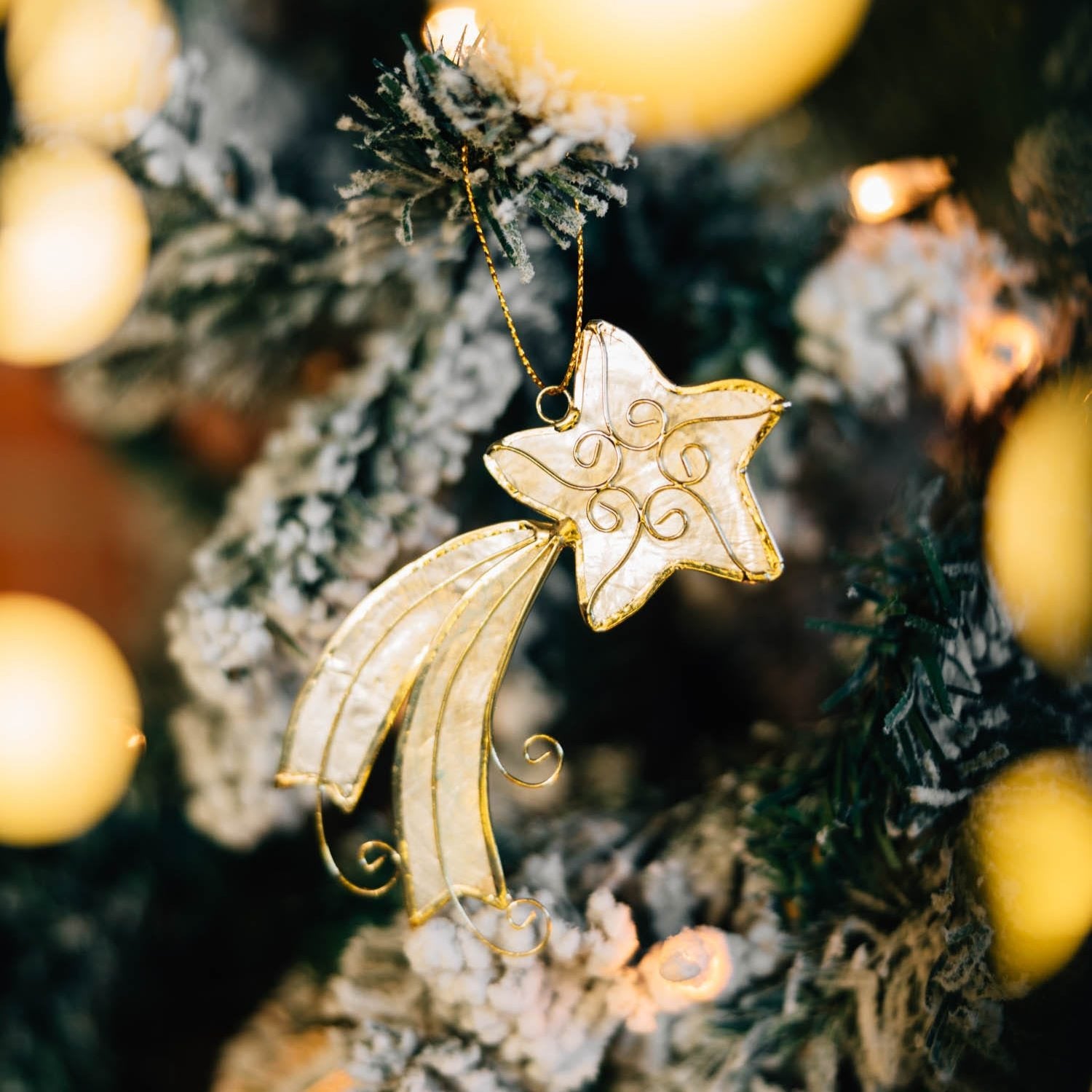 Close-up of the capiz shooting star ornament hanging on a holiday tree, showcasing its luminous shell texture.