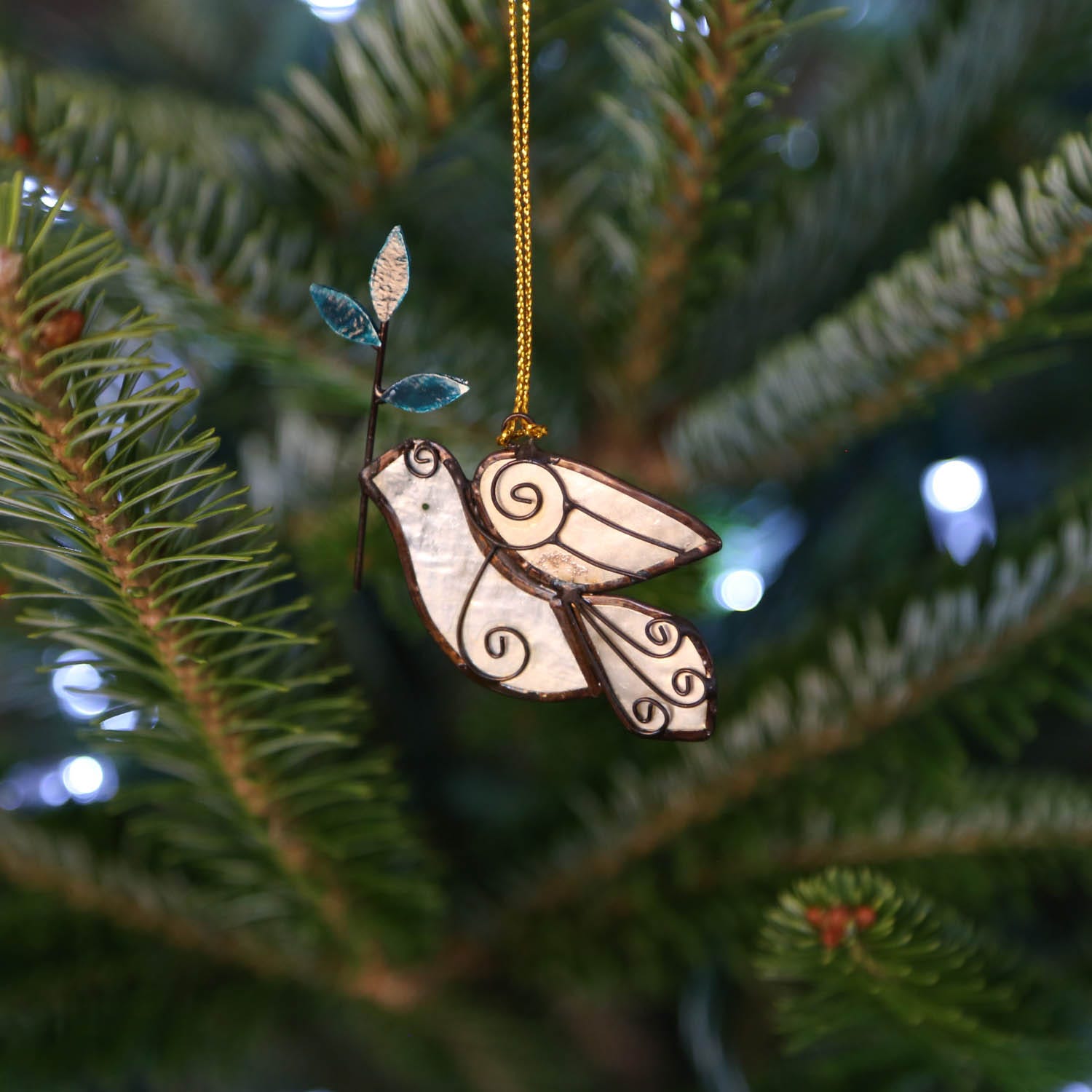 Handcrafted capiz dove ornament displayed on a holiday tree, showcasing its translucent beauty.