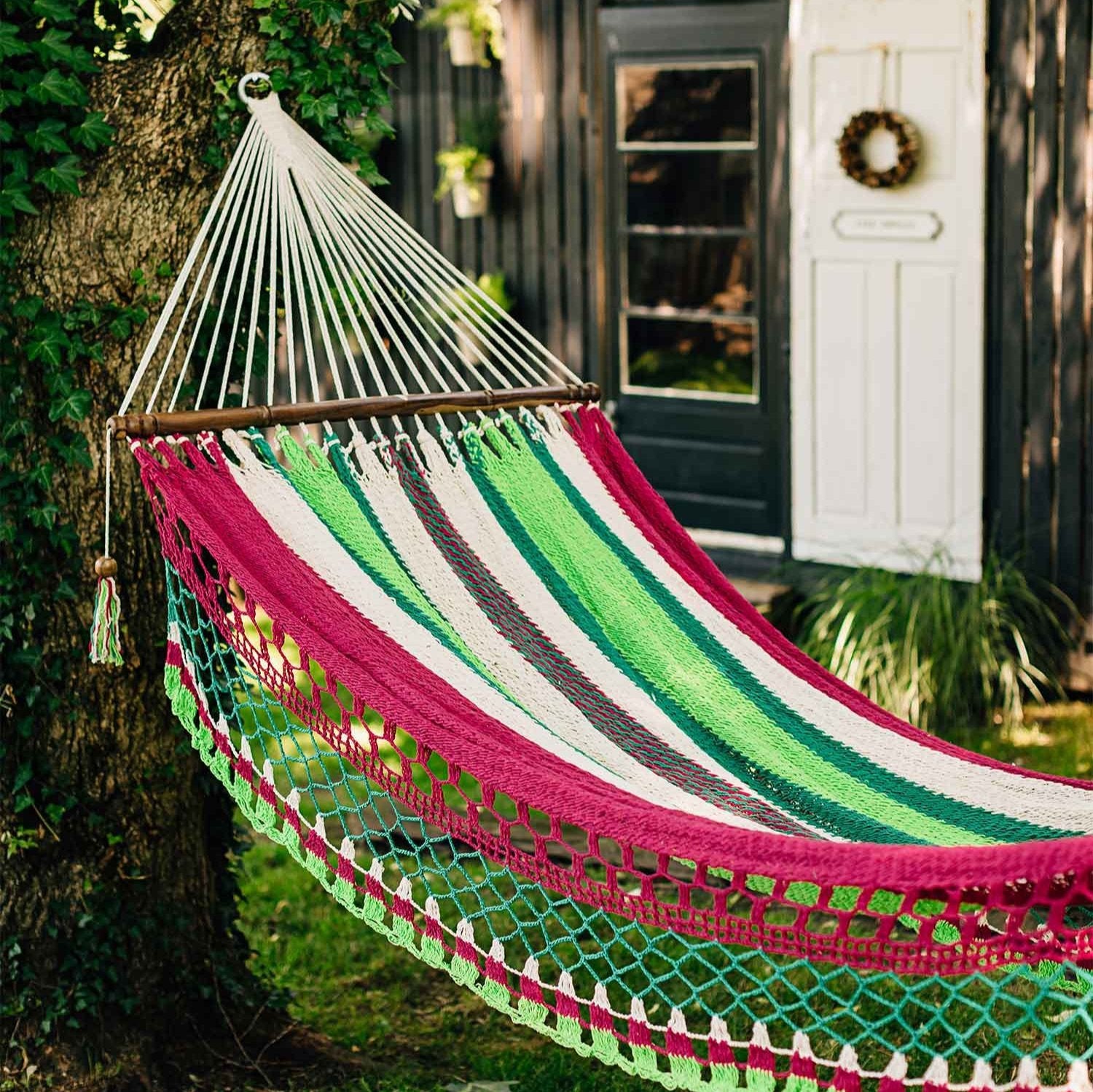 Handmade hammock with fringe hanging between two trees in a sunny backyard