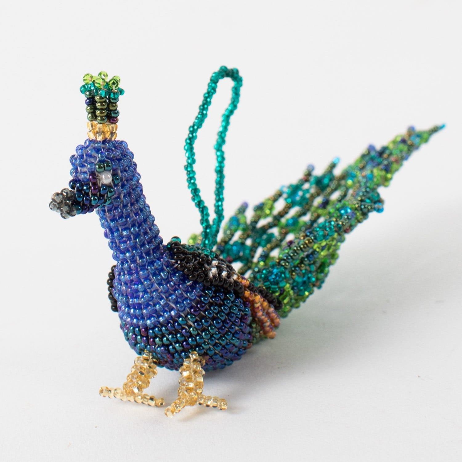 Colorful handcrafted peacock ornament hanging on a Christmas tree, showcasing traditional beadwork and vibrant colors