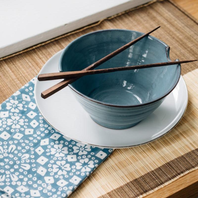 Saj wood chopsticks resting in a vibrant blue bowl